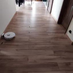 Nowo ułożone panele podłogowe w korytarzu mieszkania, z widocznym robotem sprzątającym przy ścianie i fragmentem wyposażenia kuchni w tle.