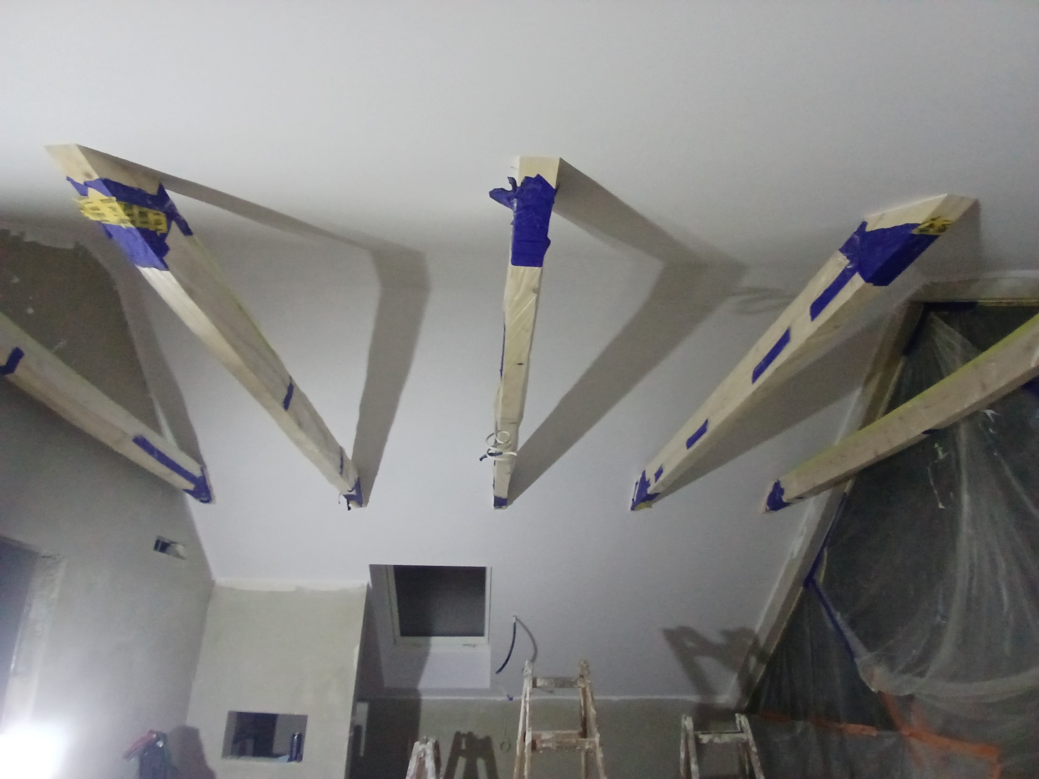 Montaż drewnianej konstrukcji pod płytę karton gips na skośnym suficie, zabezpieczonej niebieską taśmą malarską.
