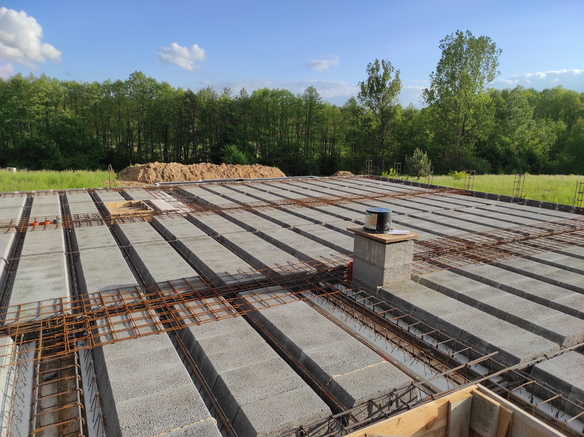 Fundament domu w trakcie budowy: szalunek, bloczki betonowe, zbrojenie stalowe, widok z góry na tle zieleni.