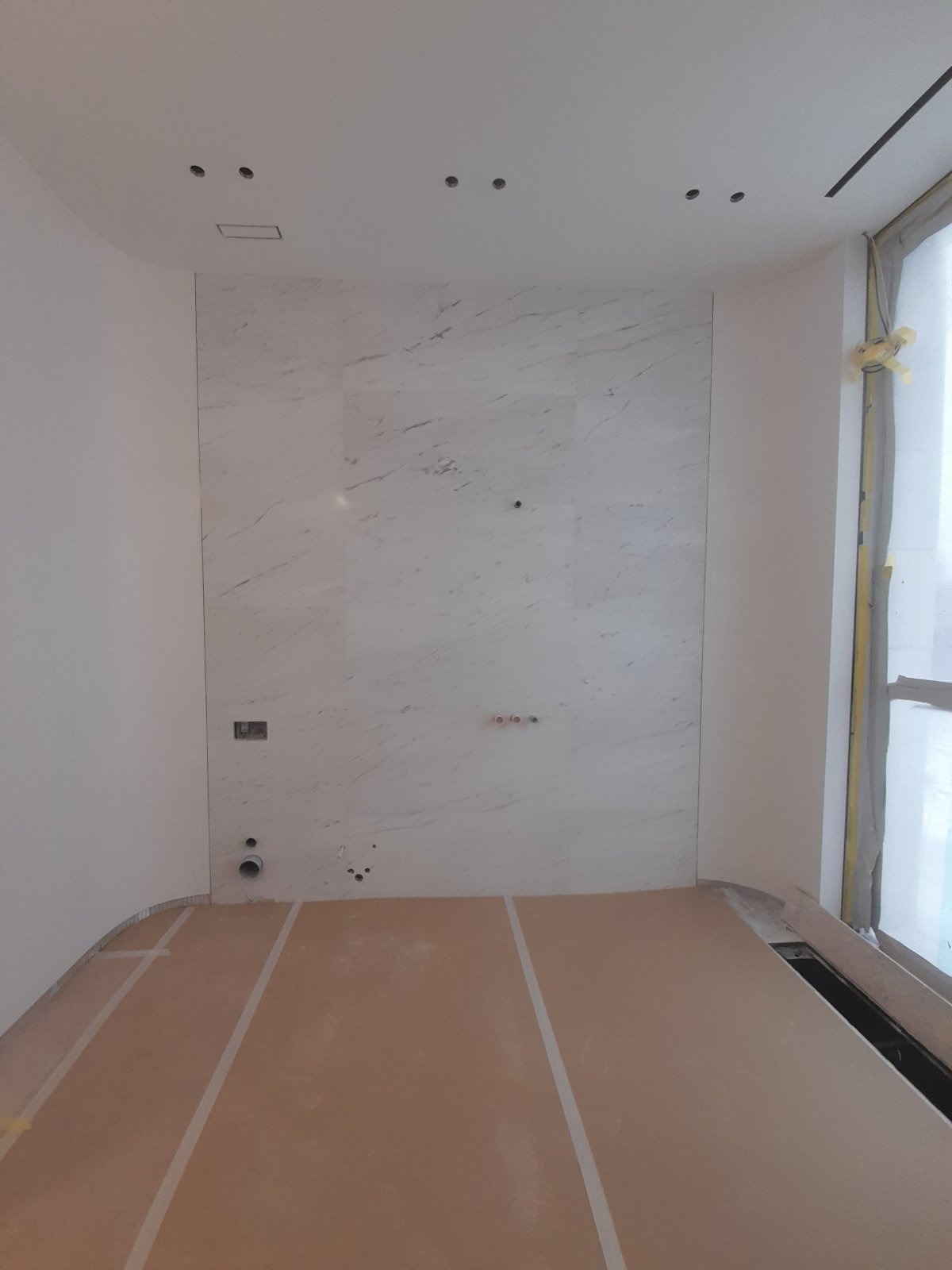 Wykończona ściana z marmurowych płyt w łazience w Łodzi. Widoczne punkty instalacji wodnej i elektrycznej. Podłoga zabezpieczona kartonem.
