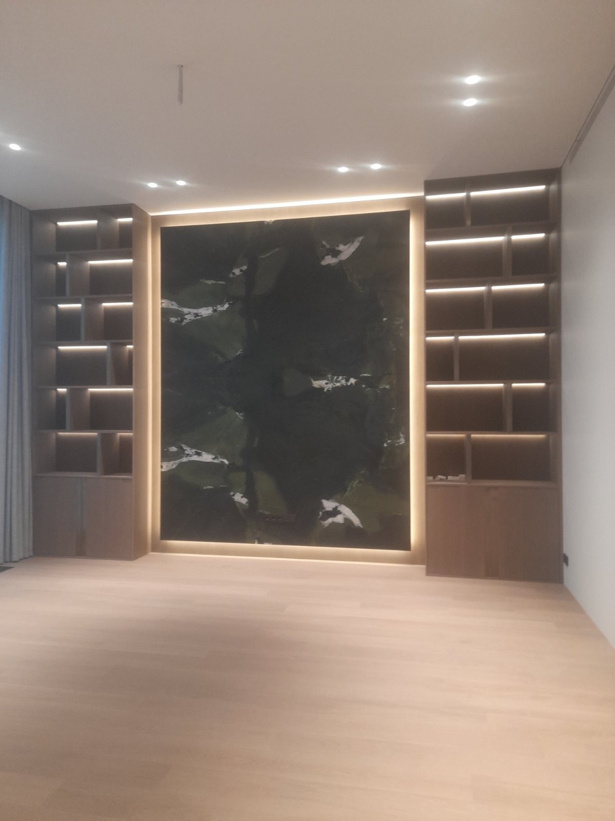 Nowoczesne wnętrze: podświetlona ściana z kamienia dekoracyjnego, zabudowane regały z oświetleniem, jasna podłoga. Minimalistyczny design, ciepłe światło.