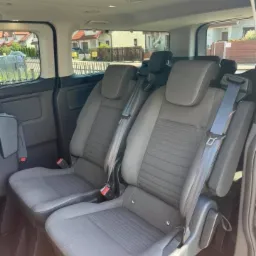 Wnętrze busa z dwoma rzędami foteli pasażerskich w szarej tapicerce, widok z boku na fotele z zapiętymi pasami bezpieczeństwa.