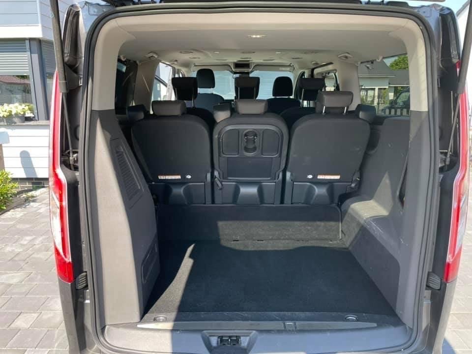 Wnętrze busa z otwartą klapą bagażnika, widoczne trzy rzędy siedzeń i przestrzeń bagażowa wyłożona czarną wykładziną.