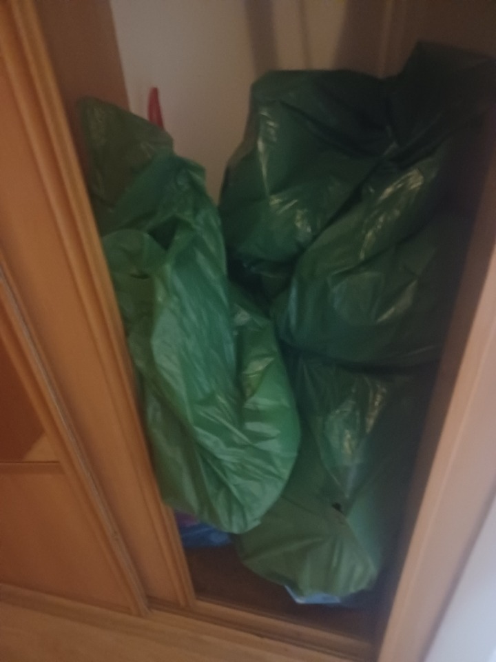 Wypełniona szafa z zielonymi workami na śmieci, prawdopodobnie po opróżnianiu mieszkania.