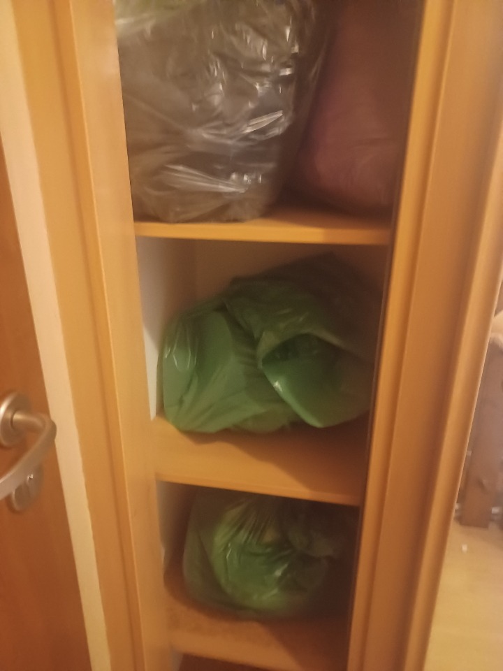 Szafa z trzema półkami wypełnionymi workami na śmieci, zawierającymi prawdopodobnie odpady po remoncie lub opróżnianiu mieszkania.