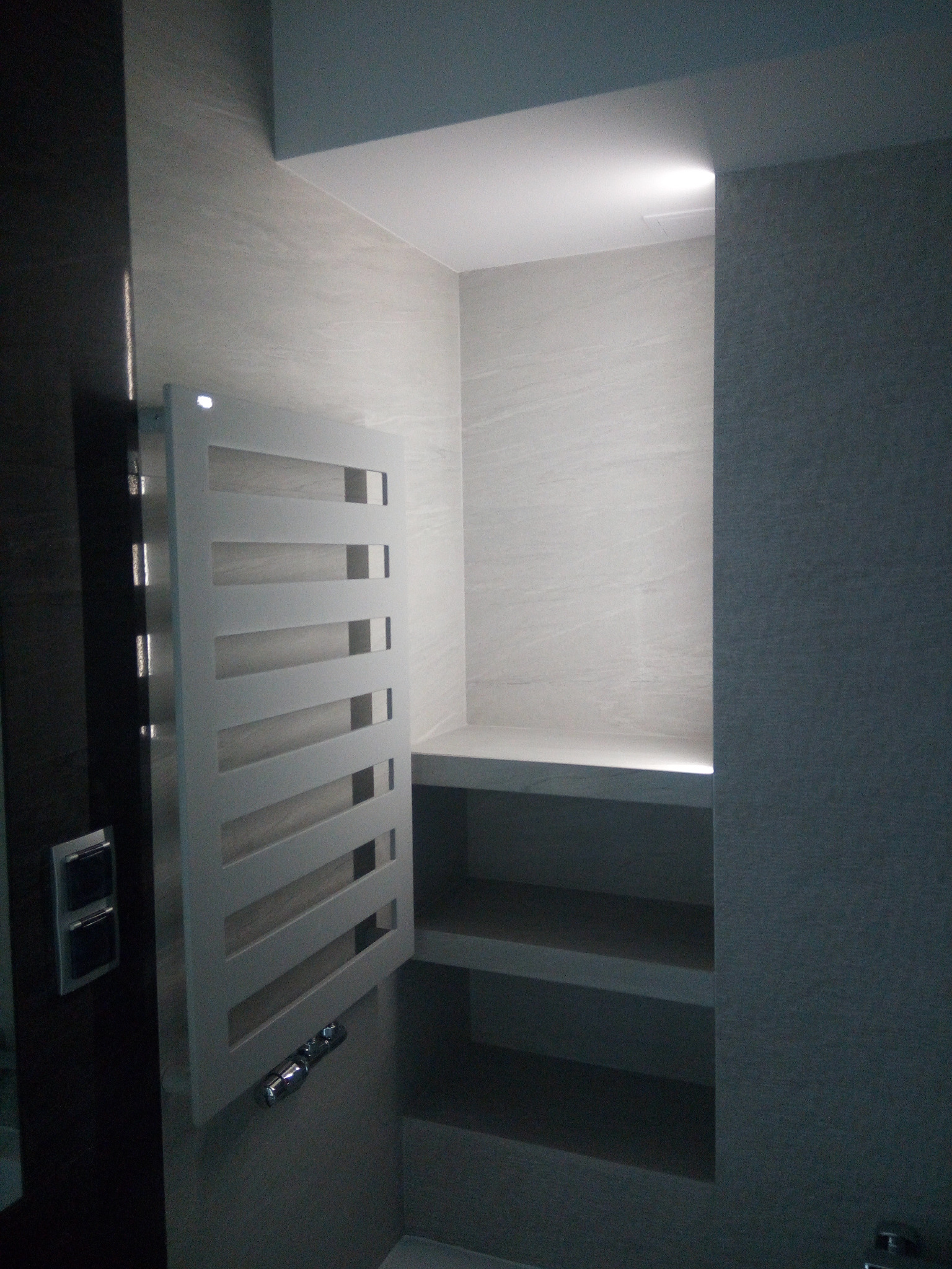 Nowoczesna łazienka z grzejnikiem drabinkowym, półkami wnękowymi i oświetleniem LED.