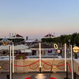 Oświetlona platforma obrotowa na czerwonym dywanie, ustawiona na tle promenady z karuzelą i budynkami o zachodzie słońca.