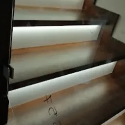 Nowoczesne schody drewniane z podświetleniem LED umieszczonym pod każdym stopniem, widoczne przez szklaną balustradę.