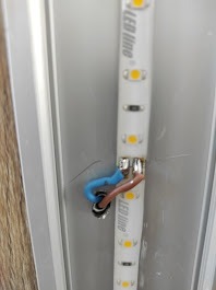 Podłączenie przewodu do taśmy LED Line w aluminiowym profilu, widoczne detale połączenia kabli: niebieski i brązowy. Element oświetlenia wnętrza.