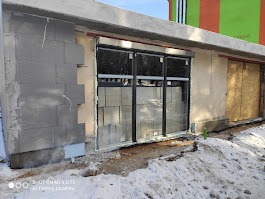 Budynek w trakcie prac murarskich z widocznym oknem i fragmentem ocieplenia. Część ściany w surowym stanie, widoczne bloczki betonowe. Zima.