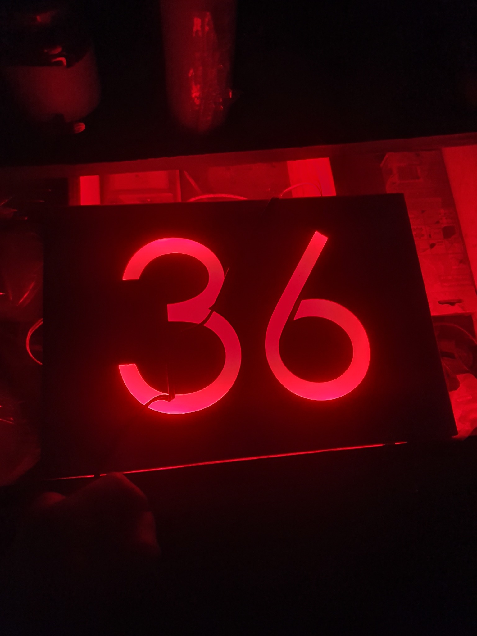 Podświetlany numer '36' w intensywnym czerwonym świetle na czarnym tle, prawdopodobnie element dekoracyjny lub numer domu.