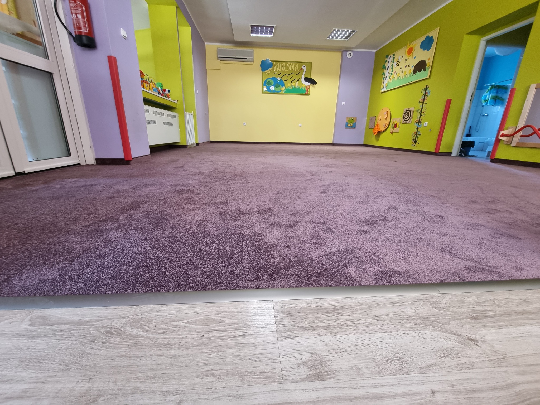 Fioletowa, pluszowa podłoga w pustym przedszkolu z kolorowymi ścianami i dekoracjami.