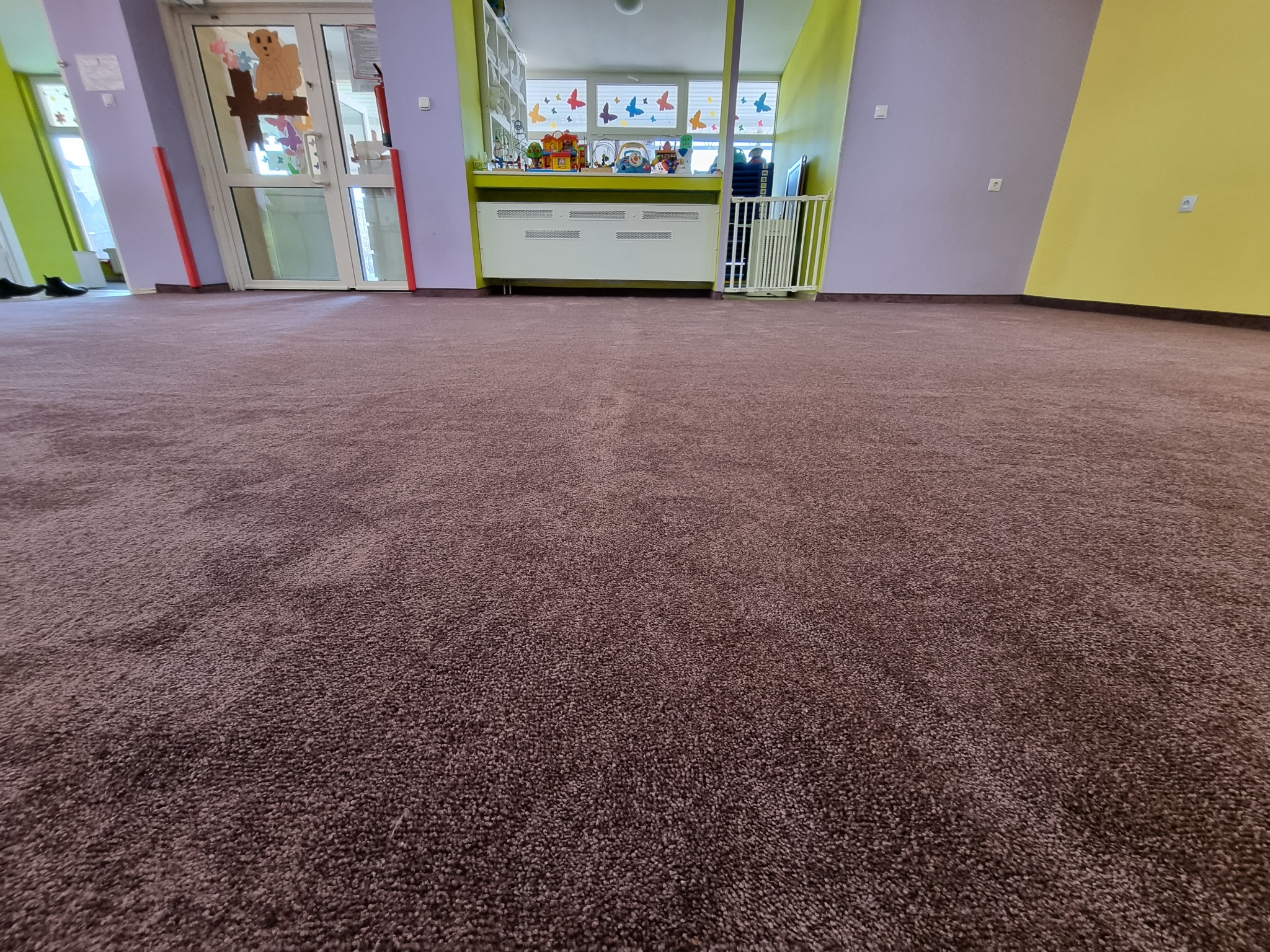 Brązowa, miękka powierzchnia w pokoju przedszkolnym z kolorowymi ścianami i zabawkami w tle.