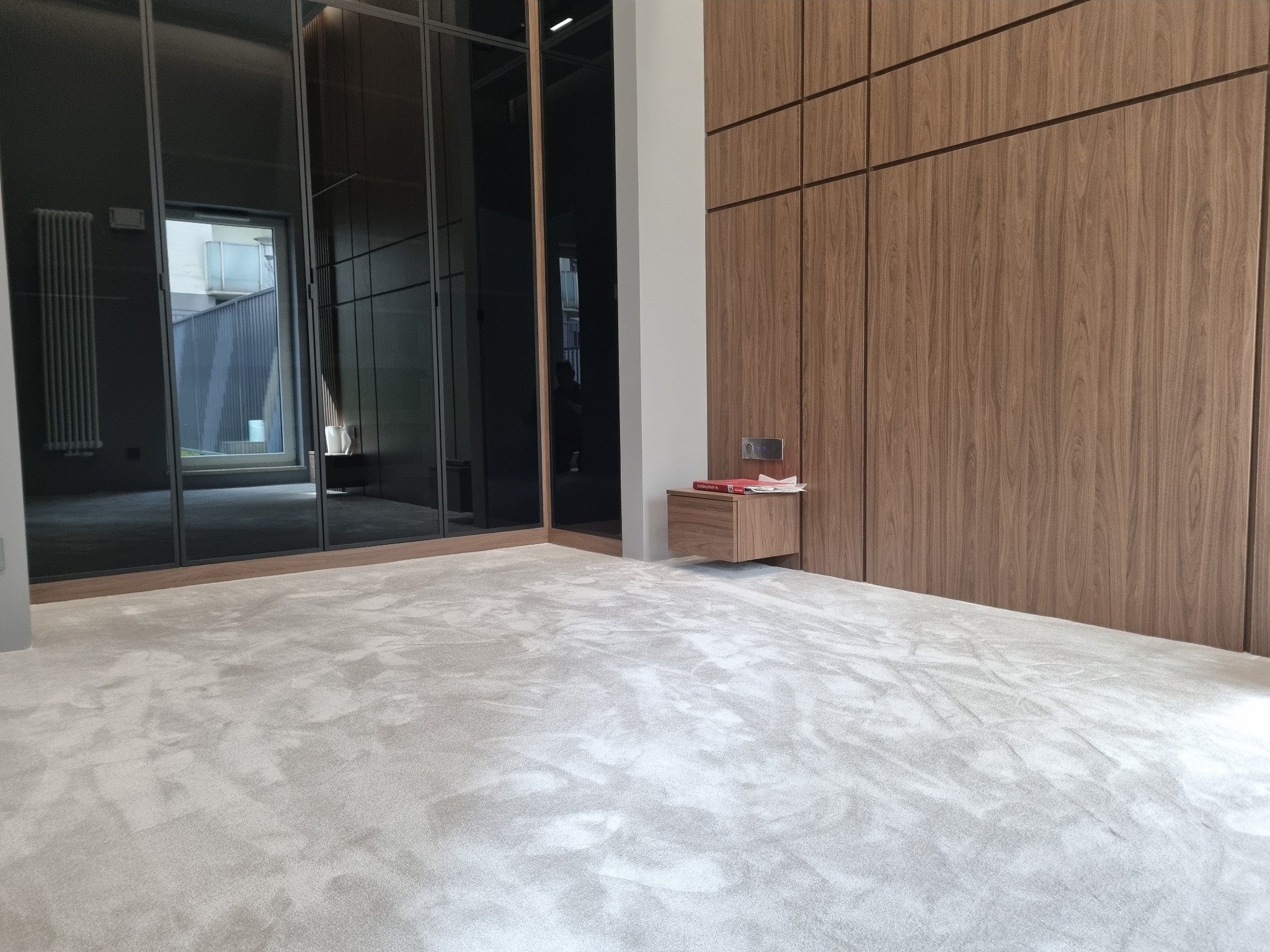 Jasnoszara, puszysta wykładzina dywanowa w pokoju z nowoczesną zabudową szaf i lustrzanym frontem, widoczny fragment szafki nocnej z książkami.