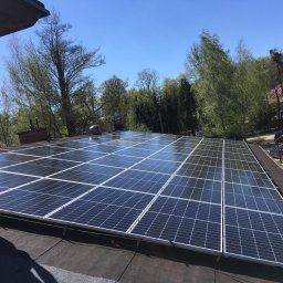 PROBO Bogusław Pabisz - Instalacja paneli słonecznych na dachu domu w słoneczny dzień, widoczny fragment sylwetki instalatora w odblaskowej odzieży roboczej i narzędzia na dachu.