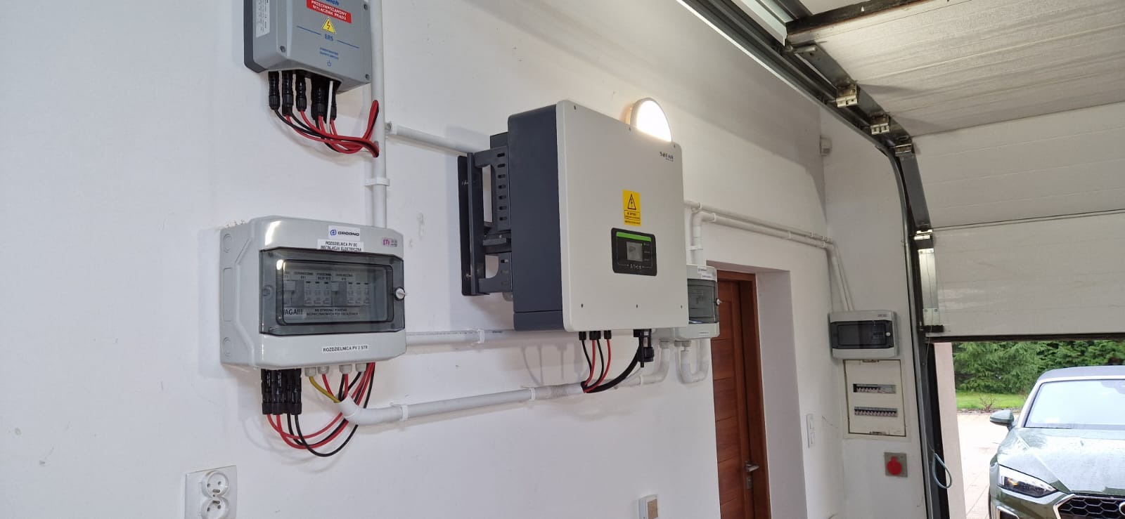Instalacja fotowoltaiczna w garażu: falownik Sofar, rozdzielnica PV DC Grodno i skrzynka przyłączeniowa. Widoczne okablowanie i zabezpieczenia.