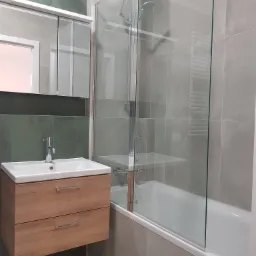 Nowoczesna łazienka z drewnianą szafką pod umywalką, szklanym parawanem nawannowym i szarymi płytkami z akcentem zieleni