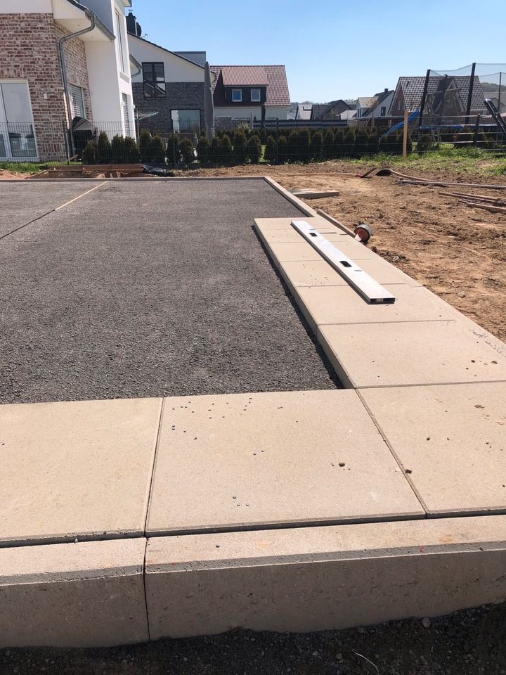 Przygotowanie podłoża pod nawierzchnię z kostki: wyrównany żwir i ułożone obrzeża z poziomnicą, widok na teren budowy i domy w tle.