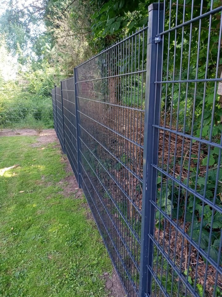 Metalowe ogrodzenie panelowe w kolorze grafitowym, widoczne z boku na tle zieleni ogrodu, z wyraźnym mocowaniem paneli do słupka.