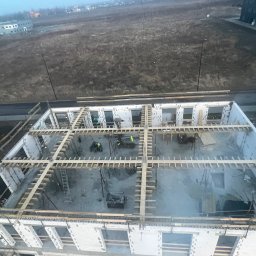 Denis Los MAXBAU - Budowa domu z betonu komórkowego: widok z góry na wznoszone ściany i drewniane szalunki stropu. Dwóch pracowników w żółtych kamizelkach na budowie.