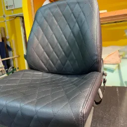 Czarne, pikowane krzesło biurowe z ekoskóry, widoczne szwy w romby, na tle warsztatu z żółtymi ścianami i materiałami.