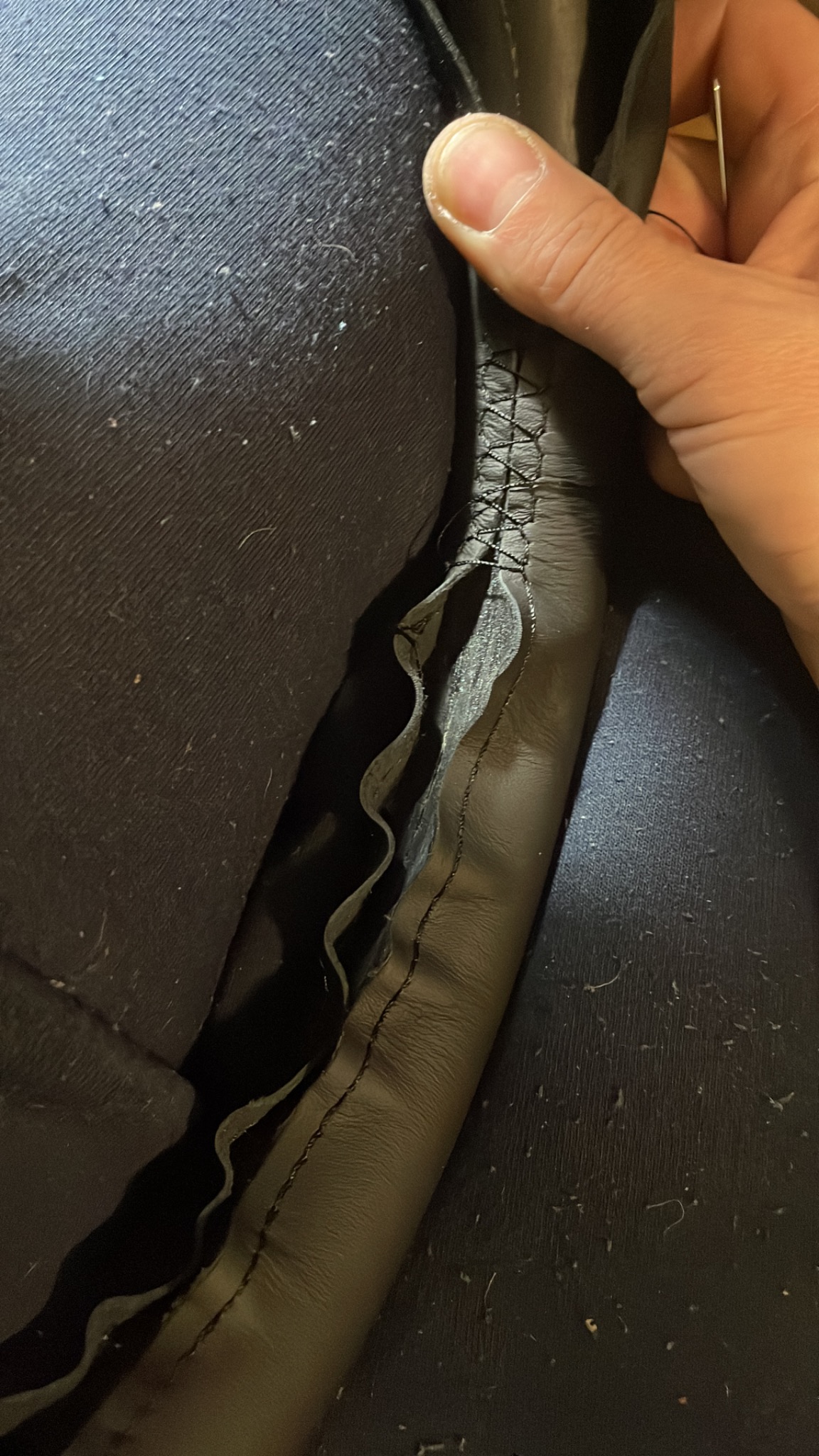 Praca ręczna: zszywanie uszkodzonego, czarnego skórzanego elementu z widoczną igłą i nicią, fragment wnętrza pojazdu w tle.