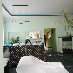 ProArt4you - Salon przygotowany do prac malarskich: meble zakryte folią i materiałem ochronnym w kropki, widoczny odkurzacz centralny, podłoga zabezpieczona czarną folią, ściany w kolorze pistacjowym.