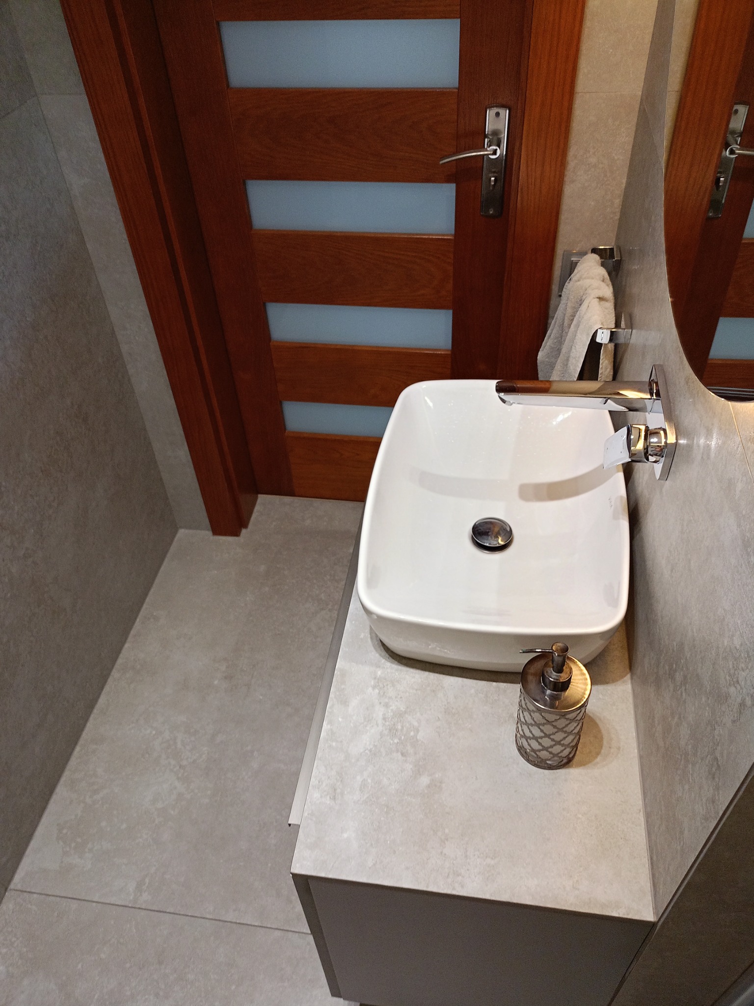 Nowoczesna łazienka z kwadratową umywalką nablatową, chromowaną armaturą, beżowymi płytkami i drewnianymi drzwiami z przeszkleniami.