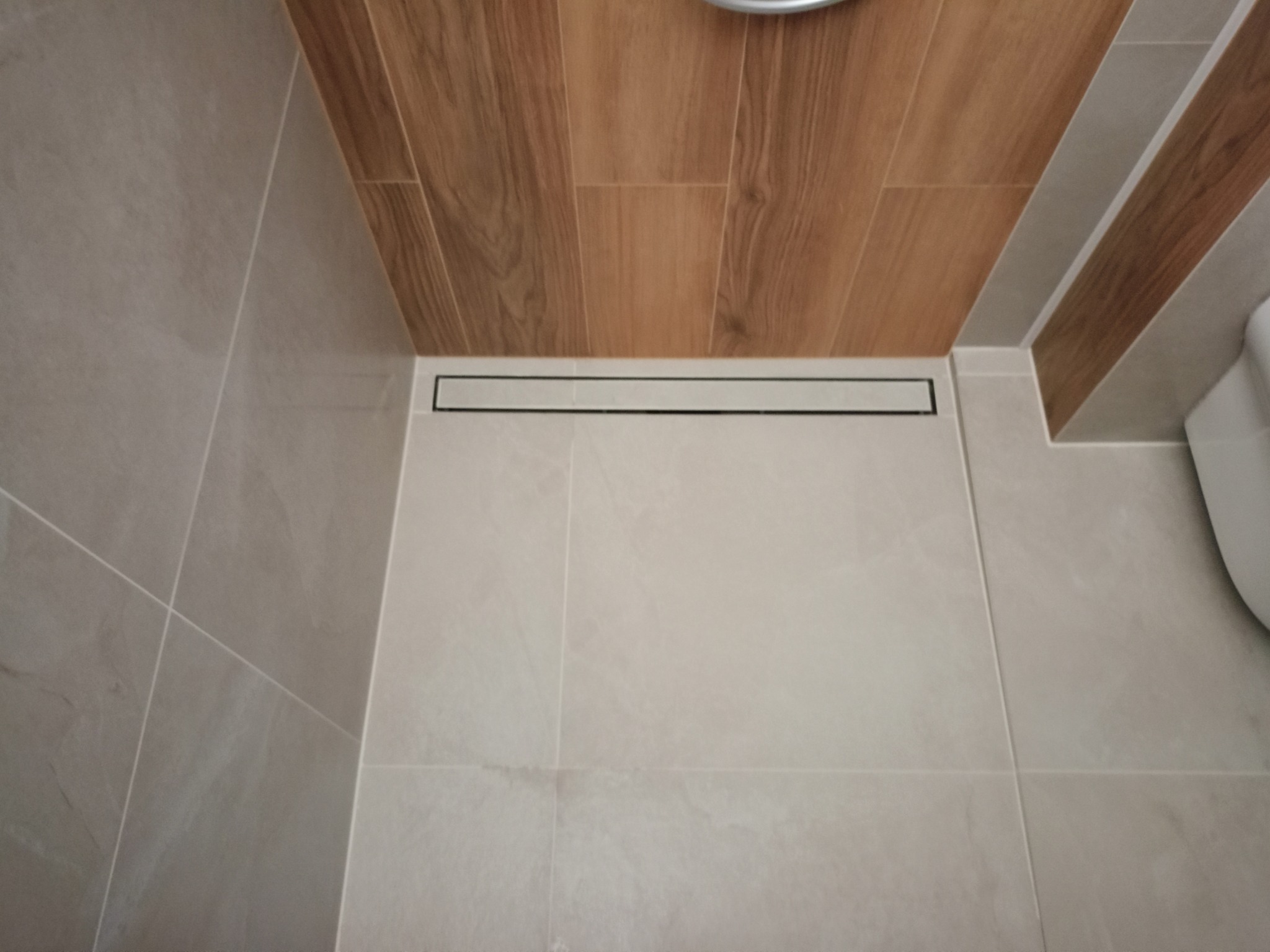 Ukończona łazienka z odpływem liniowym, płytkami imitującymi drewno na ścianie i jasnymi płytkami podłogowymi.