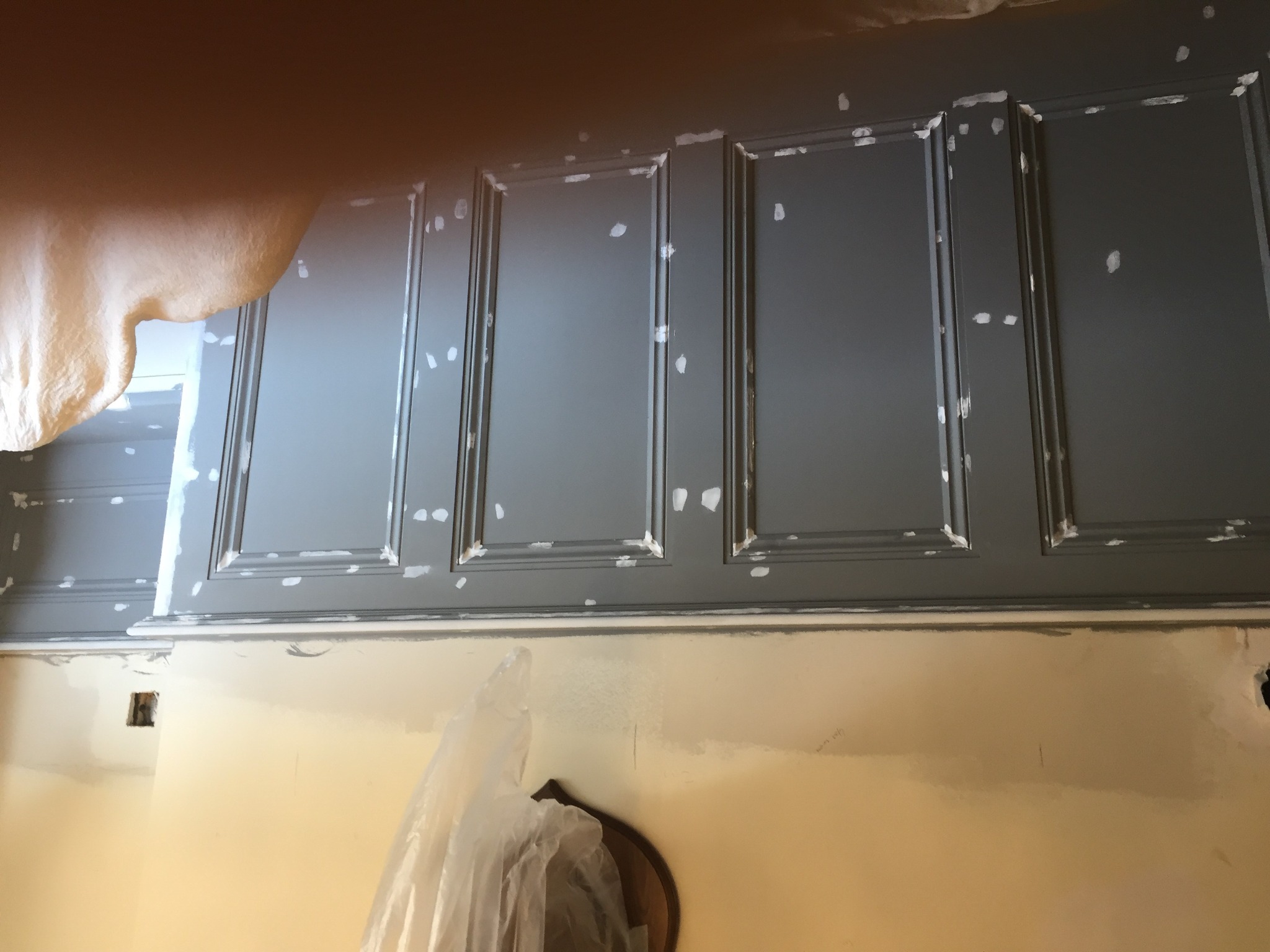 Szara boazeria ścienna z panelami w trakcie naprawy, widoczne punkty po szpachlowaniu i ślady farby na ścianie poniżej.