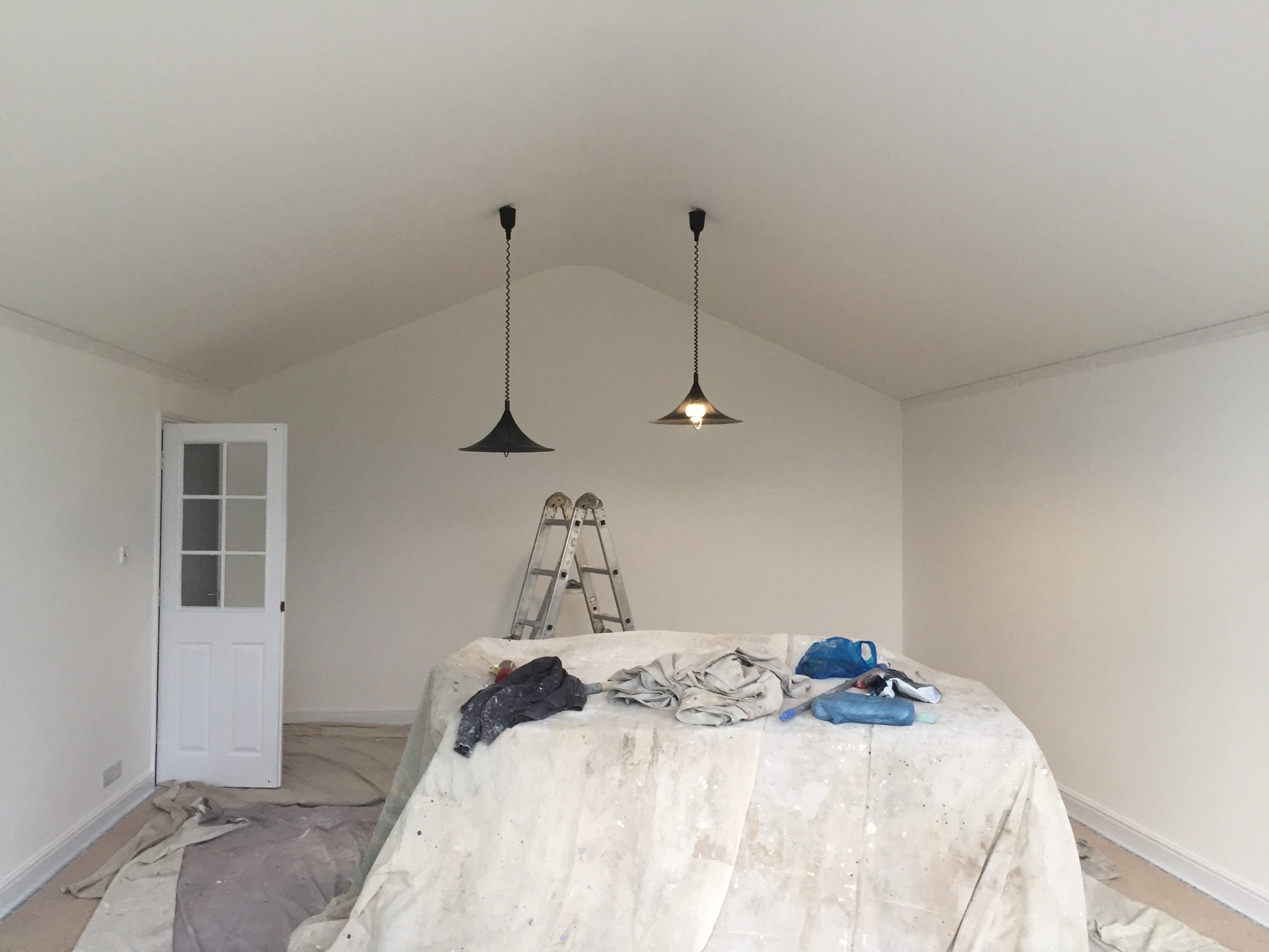 Pokój w trakcie odświeżania: świeżo pomalowane ściany w jasnym odcieniu, zabezpieczone meble pod przykryciem, drabina oparta o ścianę, wiszące lampy.