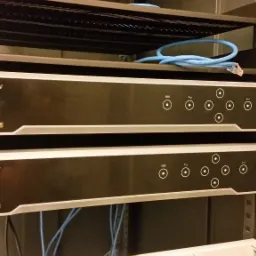 Dwa rejestratory Hikvision zamontowane w szafie rack, widoczne porty USB, przyciski funkcyjne, diody LED i niebieski kabel sieciowy na górnej półce.