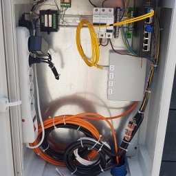 Łukasz Kołodziejczyk - ALSET-SYSTEM - Otwarta skrzynka instalacyjna z widocznym okablowaniem, listwą zasilającą, modułem światłowodowym Ultimode, przełącznikiem sieciowym Dahua, bezpiecznikami Schneider Electric oraz innymi elementami...