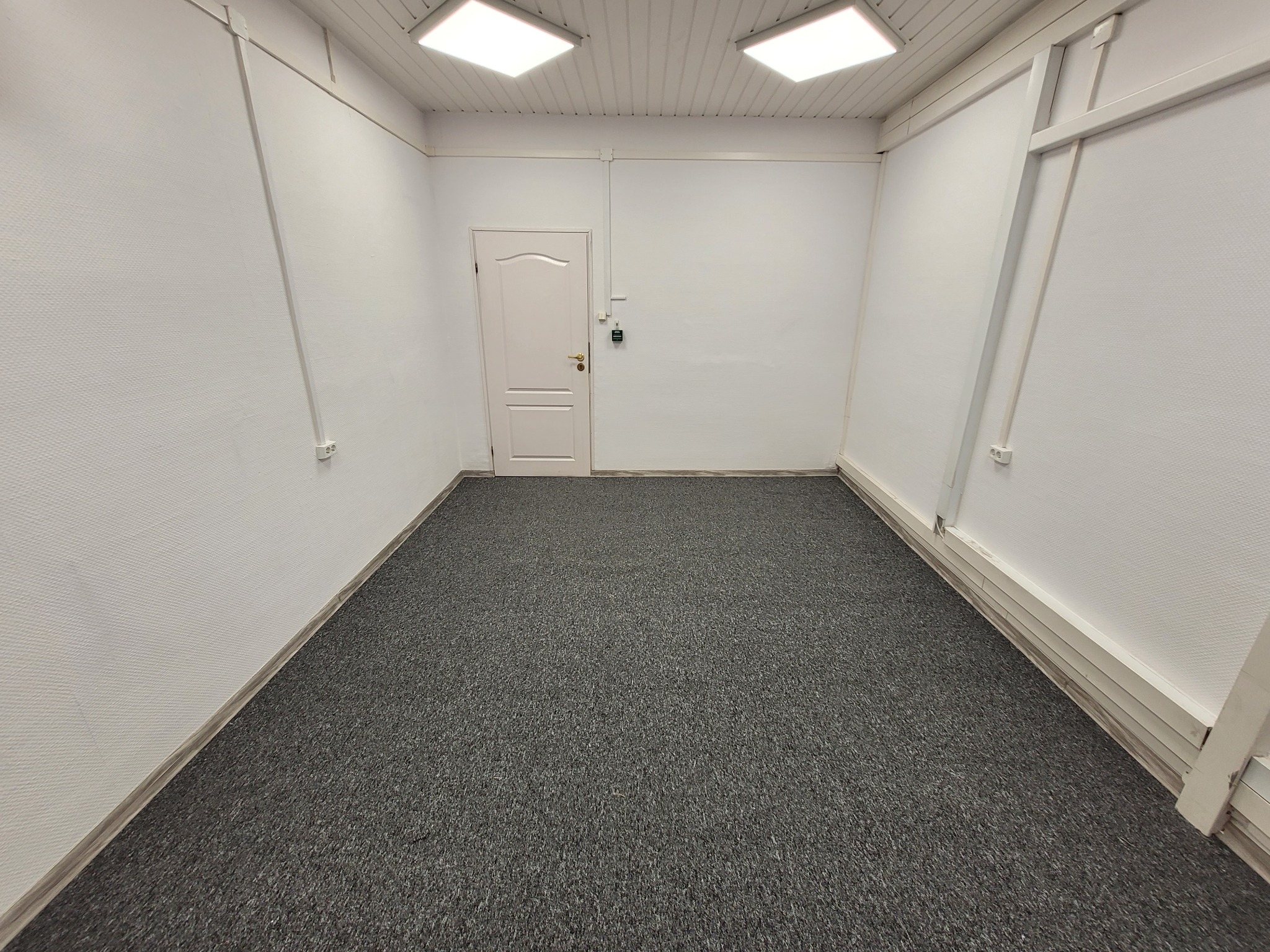 Puste, odnowione pomieszczenie z szarym dywanem, białą teksturą ścian, białą stolarką drzwiową i dwoma kwadratowymi lampami sufitowymi.