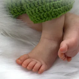 Drobne stópki noworodka na puszystym, białym tle, z zielonym, dzierganym okryciem.