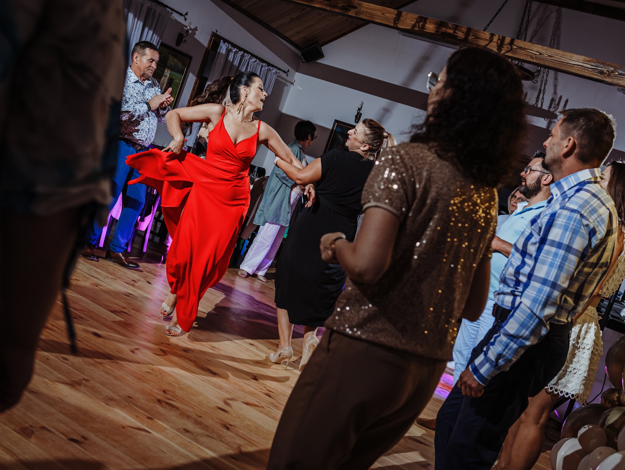 Roztańczona kobieta w czerwonej sukni na parkiecie podczas imprezy, w tle bawiący się goście.