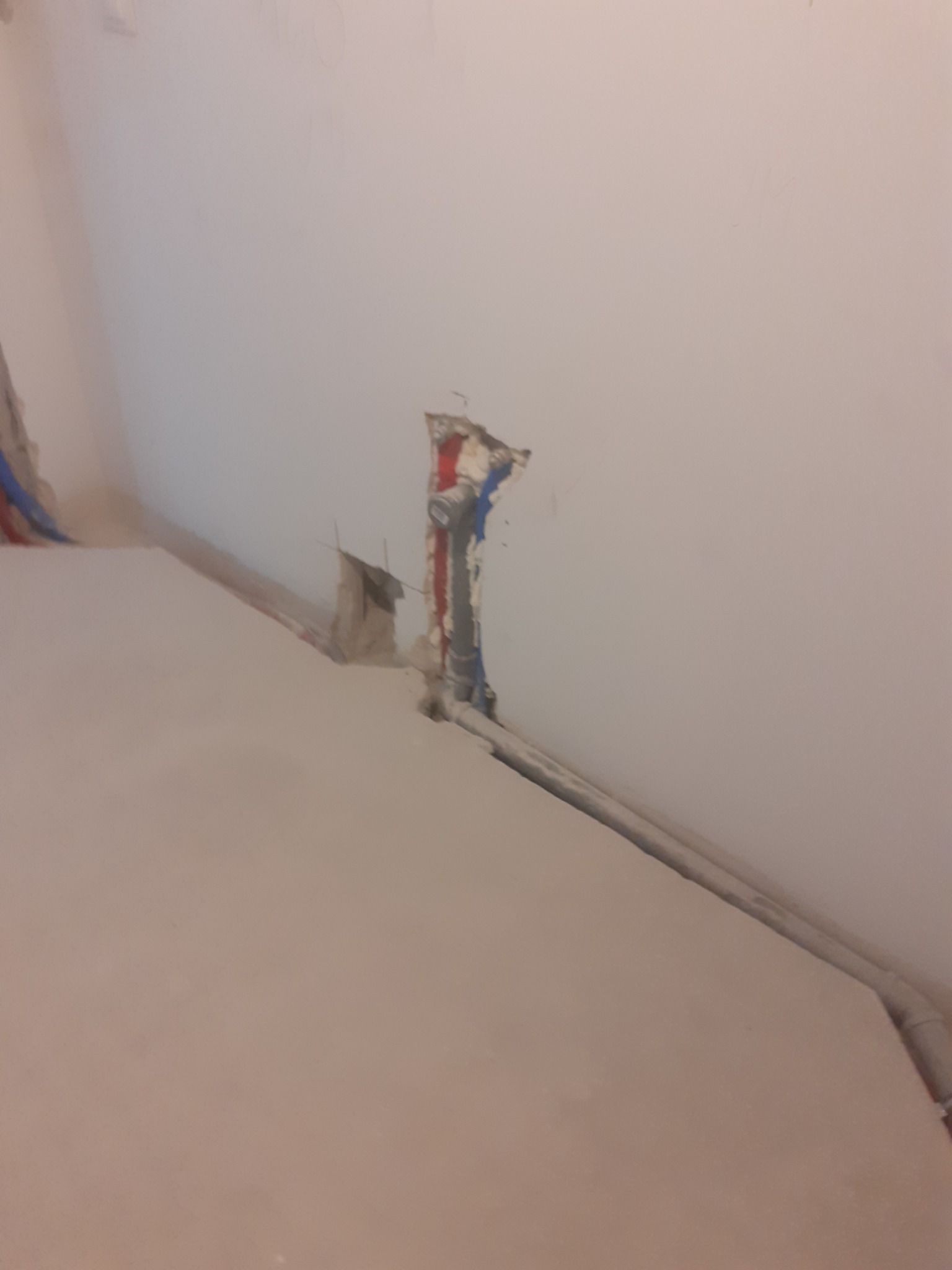 Fragment ściany z wystającymi rurami instalacji wodnej i grzewczej, widoczne ślady po kuciu w ścianie, przygotowanie do prac wykończeniowych.