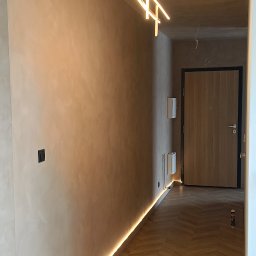 dominik florczak - Korytarz po remoncie z podświetleniem LED przy podłodze, gładzią na ścianach i nowoczesną lampą wiszącą.