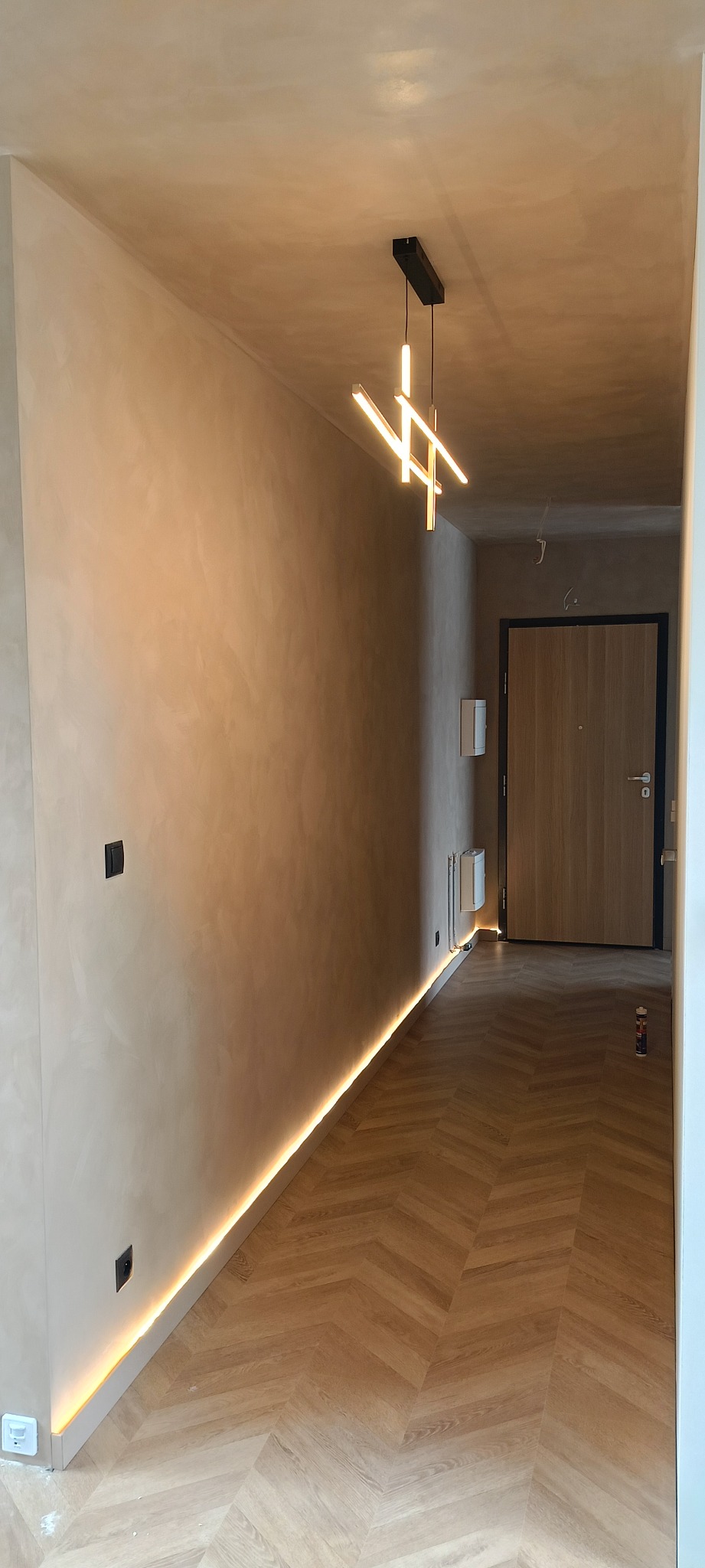 Korytarz po remoncie z podświetleniem LED przy podłodze, gładzią na ścianach i nowoczesną lampą wiszącą.