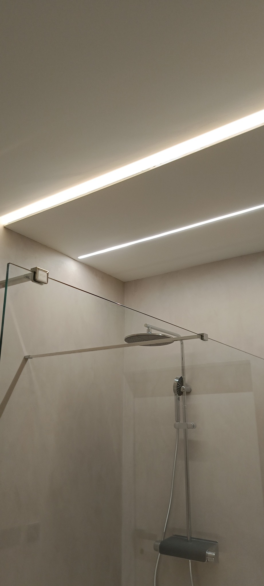 Nowoczesna kabina prysznicowa z deszczownicą i szklaną ścianką, oświetlona listwami LED w suficie, z widocznymi detalami wykończenia.