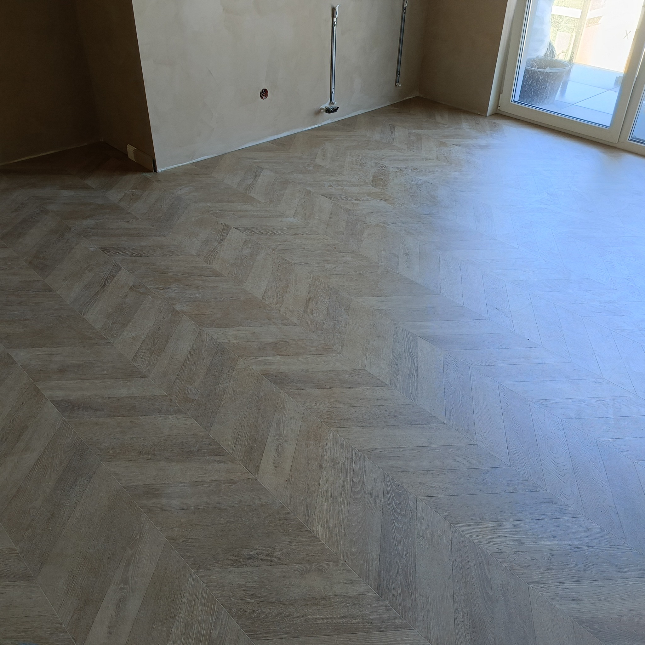 Ułożone panele podłogowe w jodełkę francuską w jasnym odcieniu drewna, ściany przygotowane do malowania z widocznymi uchwytami do grzejników.