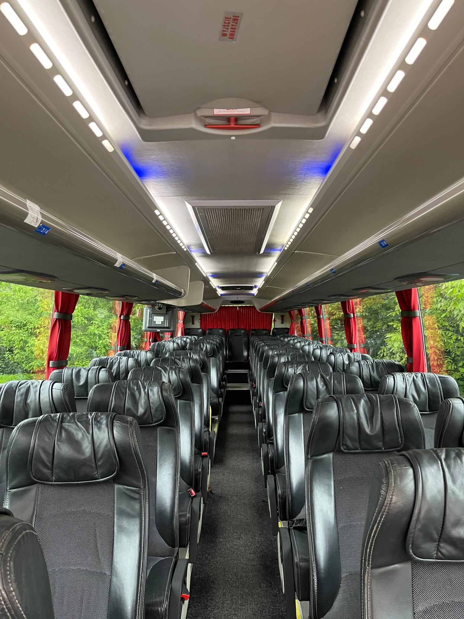 Wnętrze autobusu turystycznego z rzędami czarnych, skórzanych foteli, oświetleniem LED i widokiem na zieleń za oknami.
