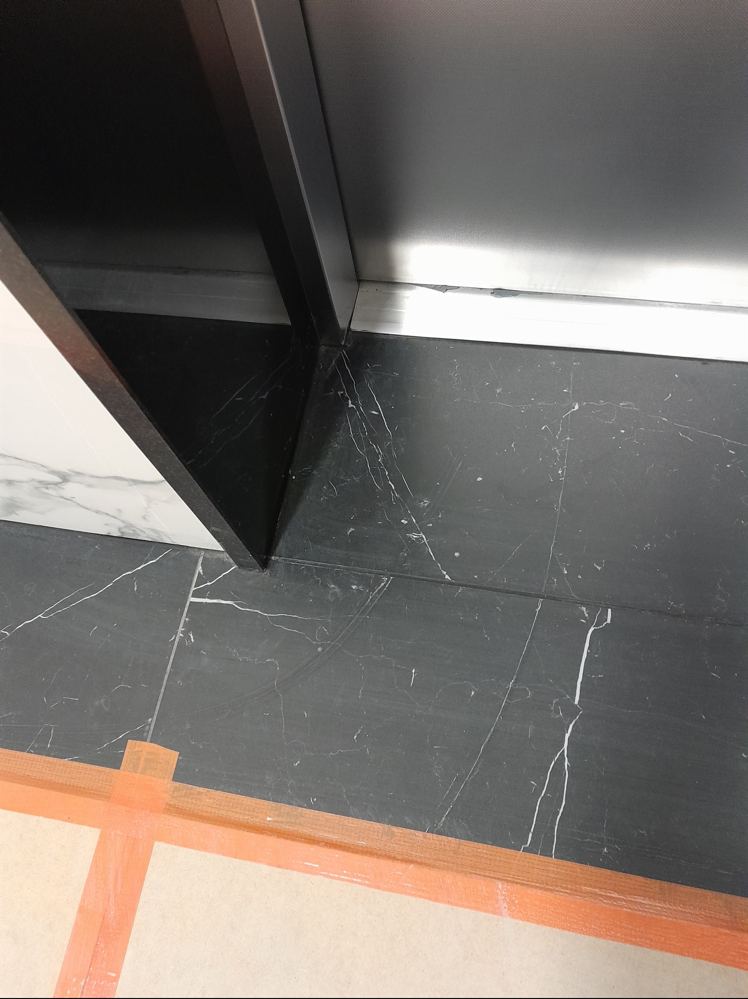 Połączenie czarnej marmurowej podłogi z białym marmurowym blatem, zabezpieczone taśmą malarską w trakcie remontu łazienki.