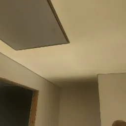 Montaż szarej płyty inspekcyjnej w suficie podwieszanym w rogu pomieszczenia, widoczny fragment ściany i osoba w czarnej koszulce.