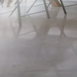 Błyszcząca, jasnoszara posadzka w trakcie polerowania, widoczne odbicia stojaków lub nóg meblowych, lekko zamglone ujęcie z niskiej perspektywy.