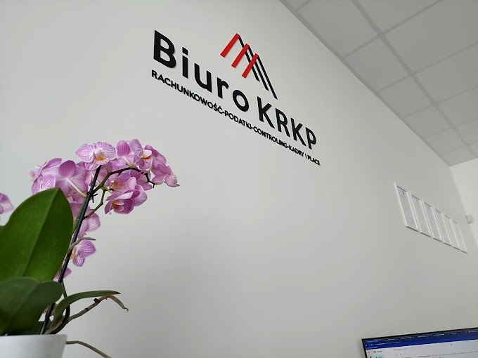 Logo biura rachunkowego KRKP na białej ścianie, z dekoracyjną orchideą w doniczce po lewej stronie i kratką wentylacyjną w tle.