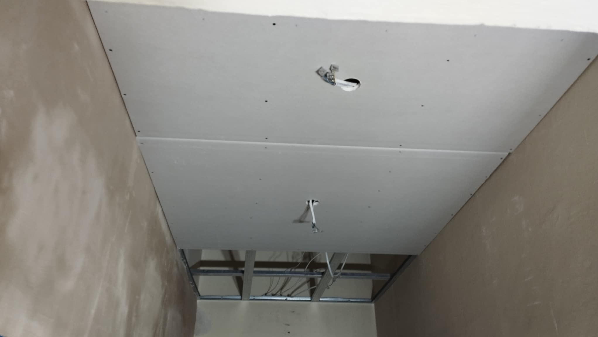 Montaż sufitu podwieszanego z płyt kartonowo-gipsowych w Mysłowicach, widoczne profile metalowe i otwory na oświetlenie.