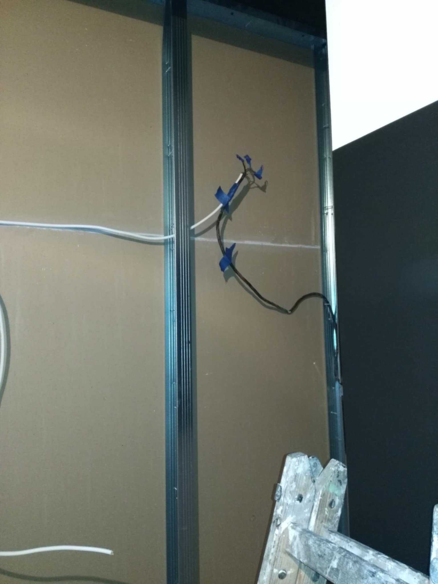 Montaż płyty karton gips na metalowym stelażu, widoczne przewody elektryczne zabezpieczone niebieską taśmą, fragment drewnianej drabiny malarskiej.