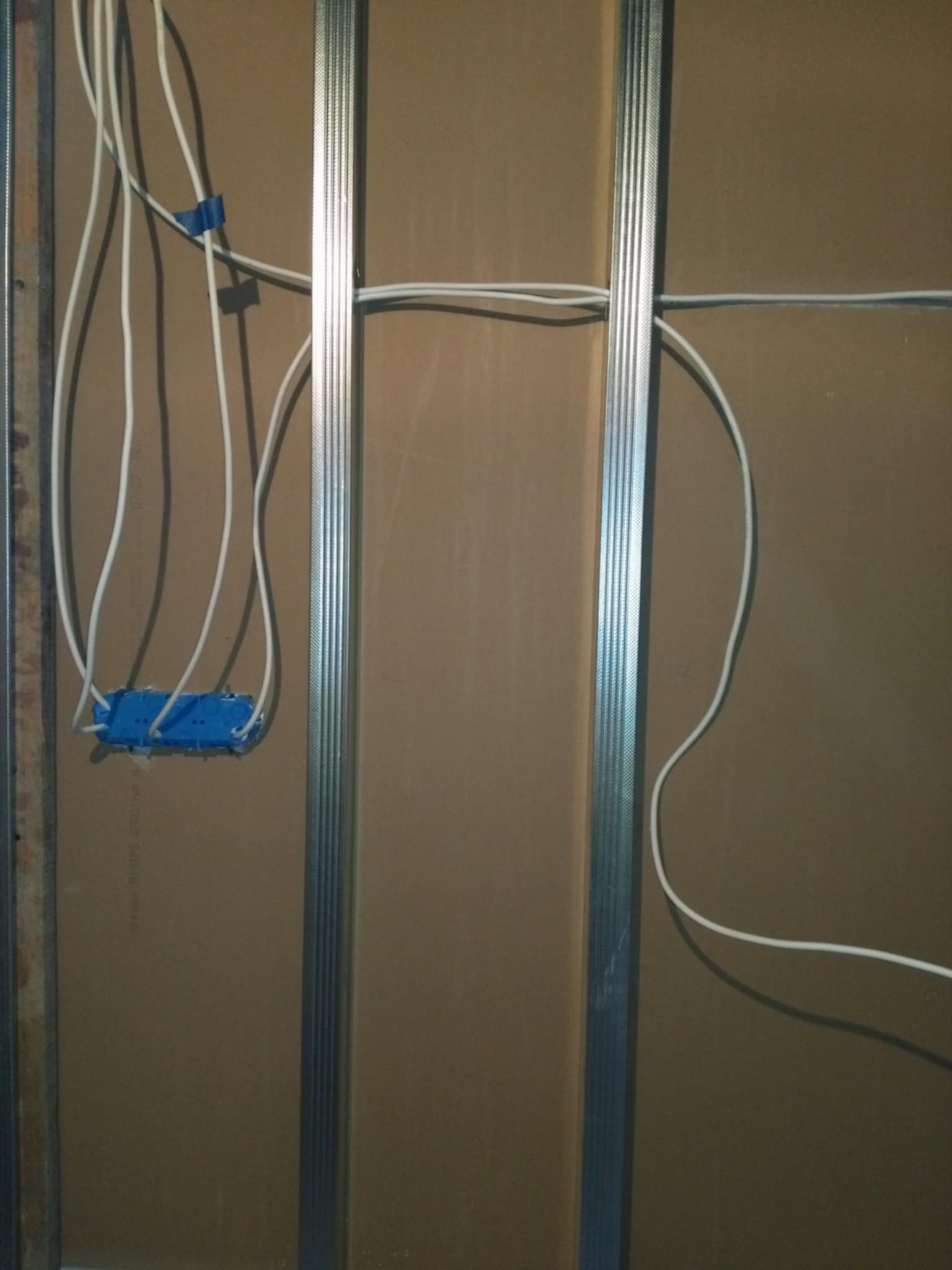 Montaż instalacji elektrycznej wewnątrz ściany z płyty karton gips, widoczne kable i metalowe profile.
