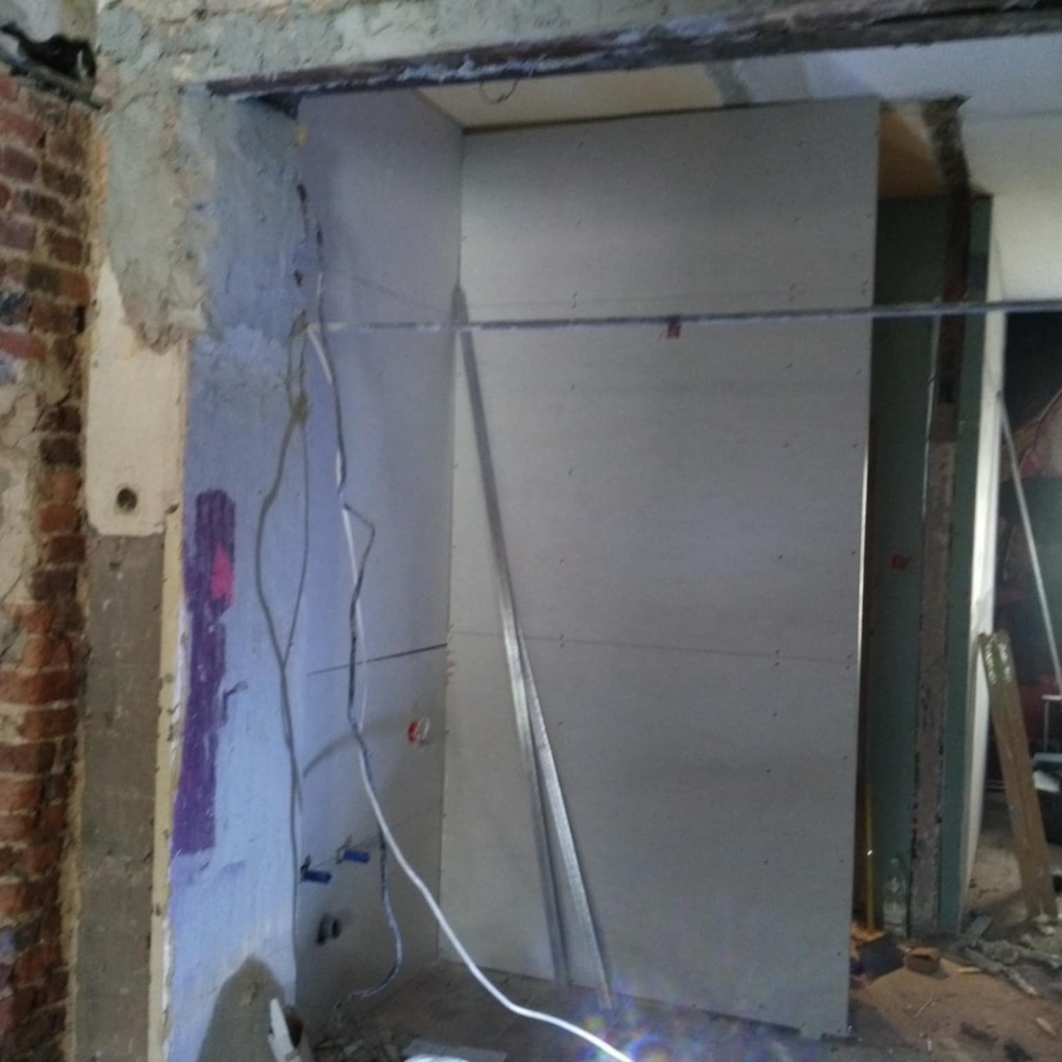 Montaż płyty gipsowo-kartonowej w trakcie prac wykończeniowych; widoczne przewody elektryczne i fragment ściany z cegły.